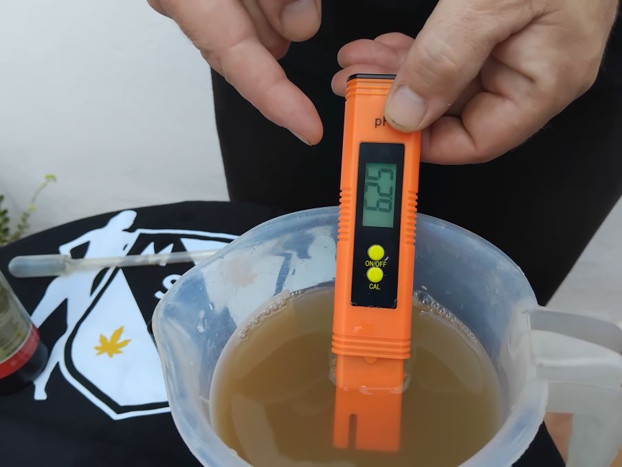 cannabis world news organic grow image of hand holding a pH pen in a container of grow nutrient liquod